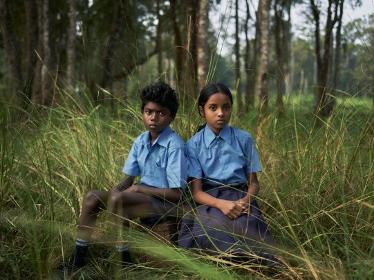 two indian children sitting in a forest