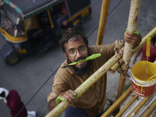 man with glasses holds a brush between his teeth and climbs a structure