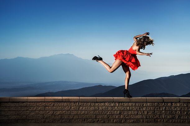 Woman in red dress and high heels dancing on a brick wall