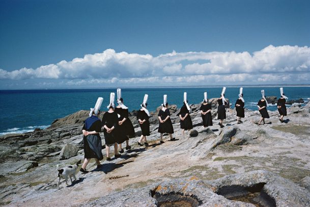 Breton women with their traditional hats and a dog queued near the sea