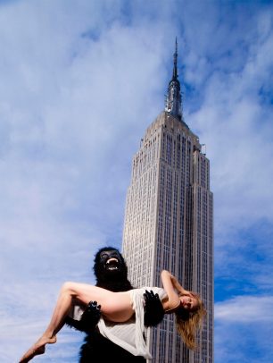 Person with monkey costume holding a girl with white dress and Empire State Building on the background