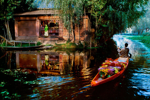 A flower vendor rowing next to a shop on a lake