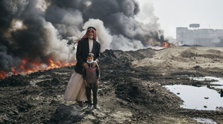 a fire with black smoke behind an old man and a child in Iraq