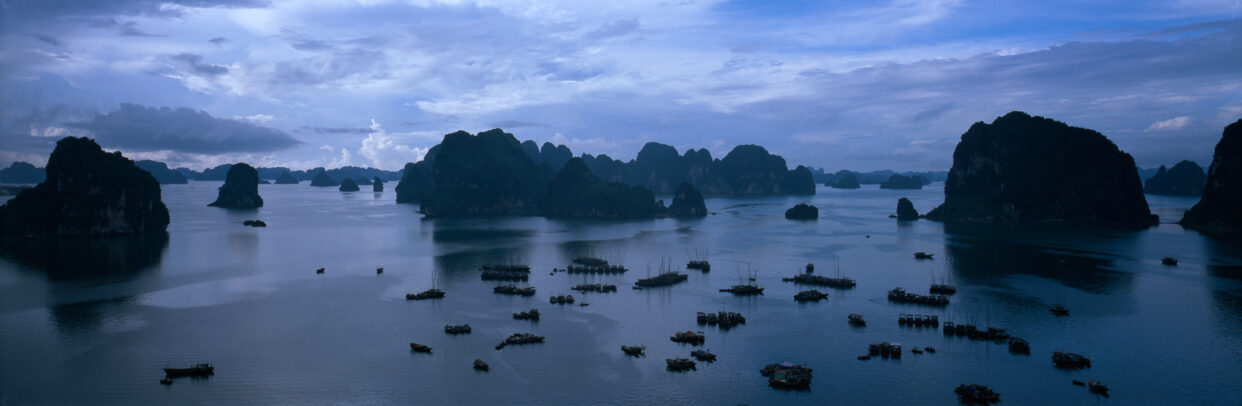 Groups of fishing boats dot the placid waters of Halong Bay