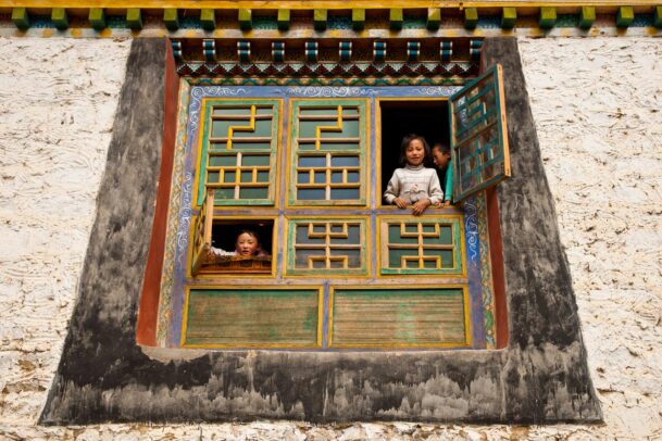 Children peer from intricately decorated windows, framed by traditional Tibetan architecture