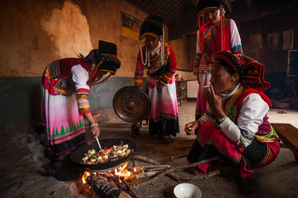 Yi wome prepare a meal at the fireplace in their village