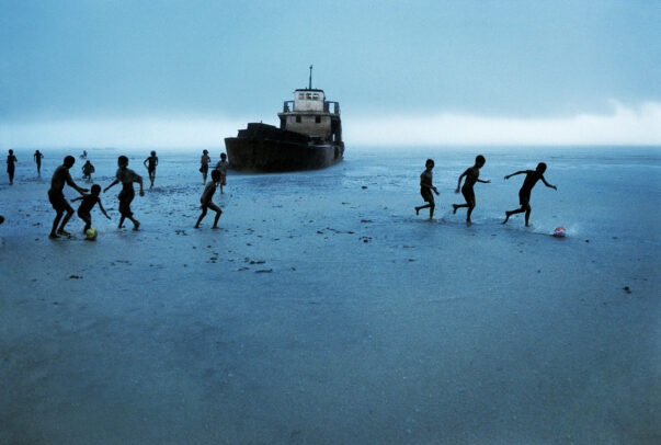 children playing football on the beach near a ship